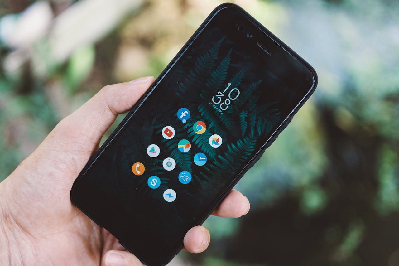 Services-02 Close-up of a hand holding a smartphone with app icons and a nature wallpaper.